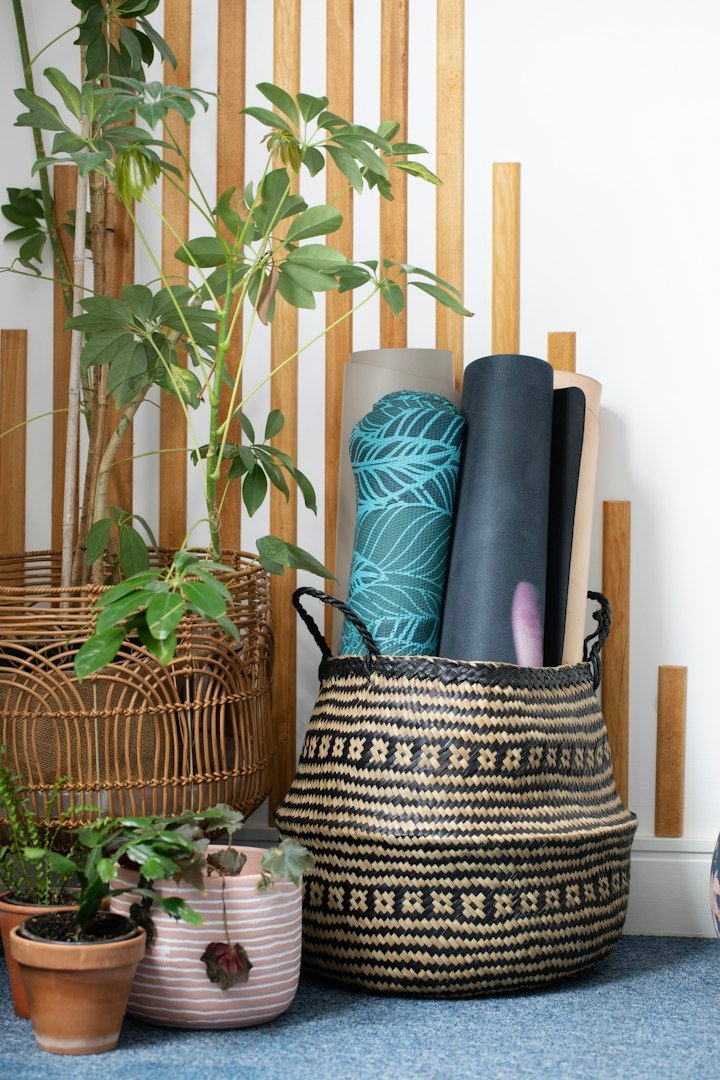 Rolled yoga mats in a woven basket beside plants, an illustrative wellness-tool scene rather than an exact product listing